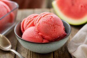 Cremiges Wassermelonen-Sorbet ohne Eismaschine in einer weißen Schüssel, mit frischer Minze garniert, auf Holztisch im Sonnenlicht