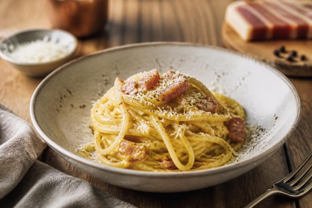 Spaghetti Carbonara im Teller angerichtet mit knusprigem Guanciale, frisch gemahlenem schwarzen Pfeffer und geriebenem Pecorino Romano
